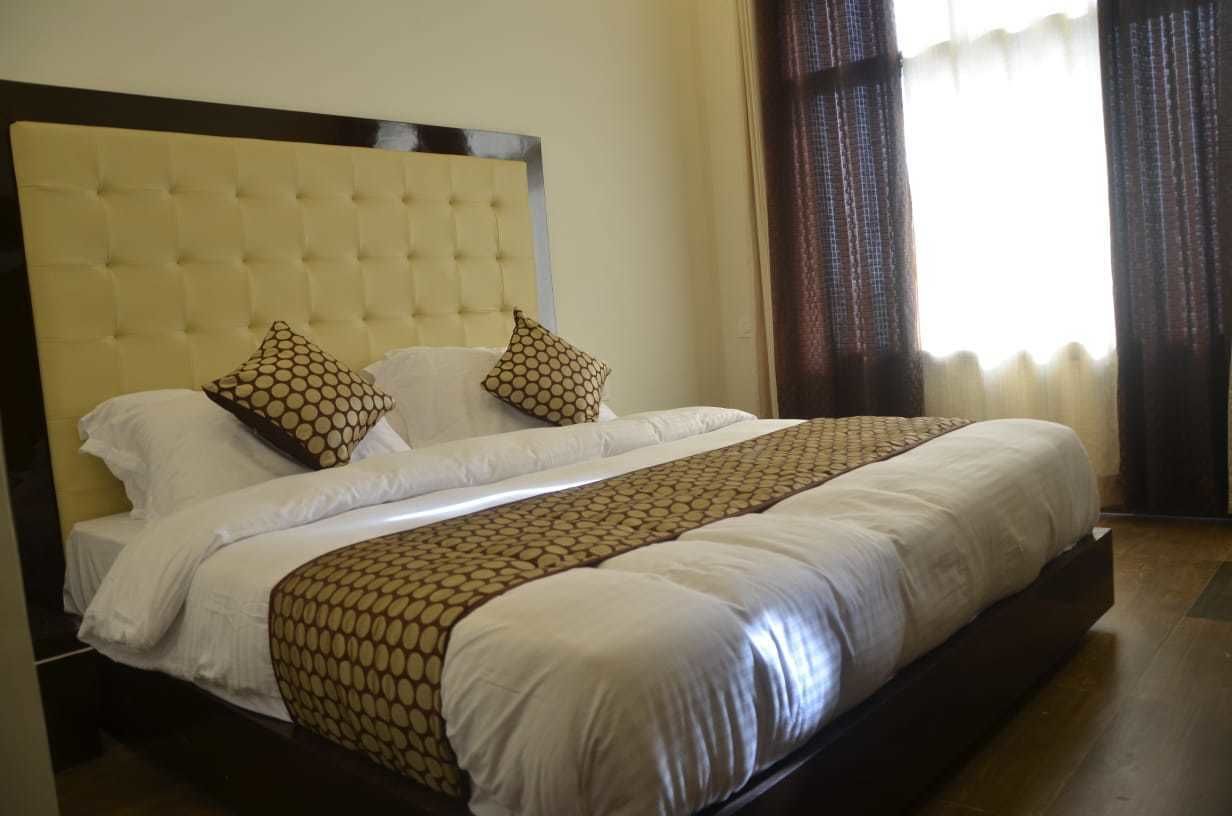 A neatly made bed with a patterned bedspread and two decorative pillows, a tufted headboard, and a view of a window with curtains.