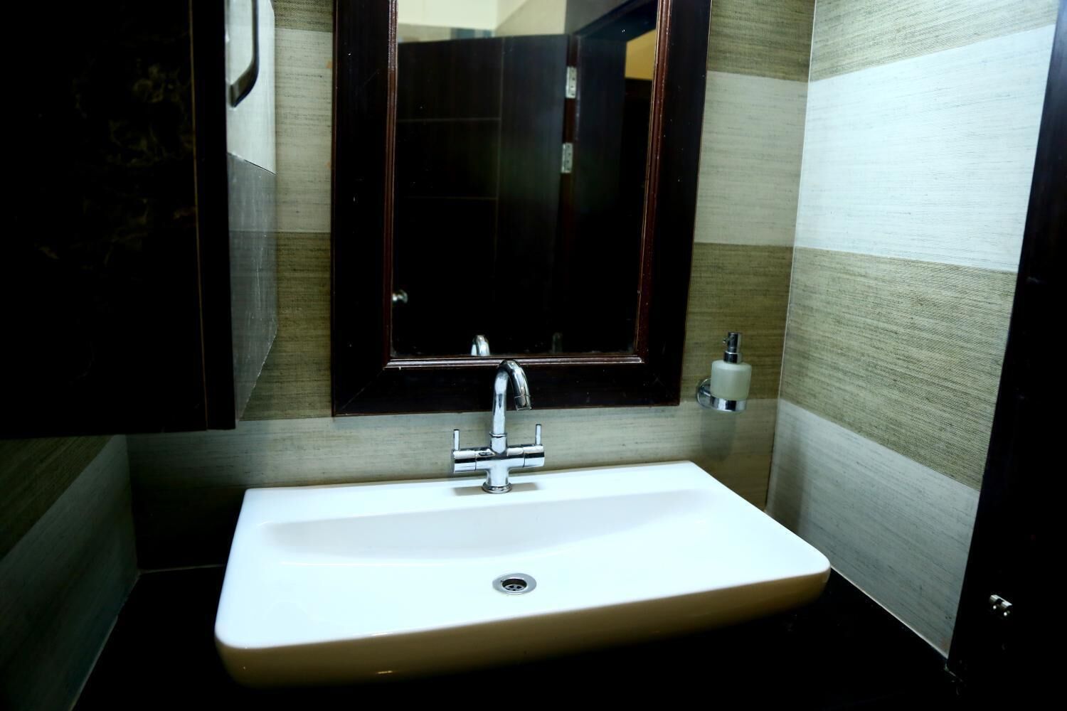 A bathroom with a white sink, a mirror, and a soap dispenser.
