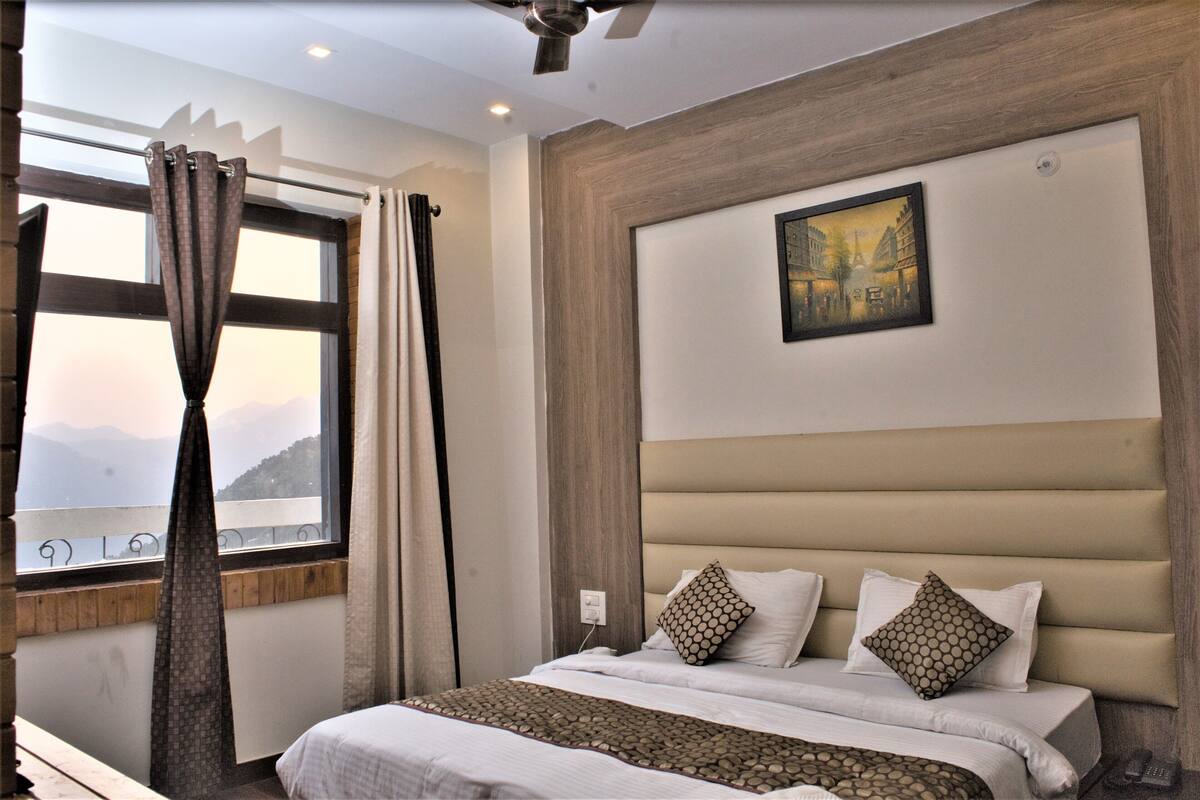 A hotel room with a large bed, a painting on the wall, and a window with curtains.