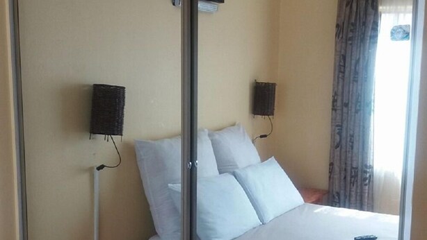 Une chambre d’hôtel avec un lit, une table de chevet en bois, un bureau, une chaise, un miroir et un tableau au mur.