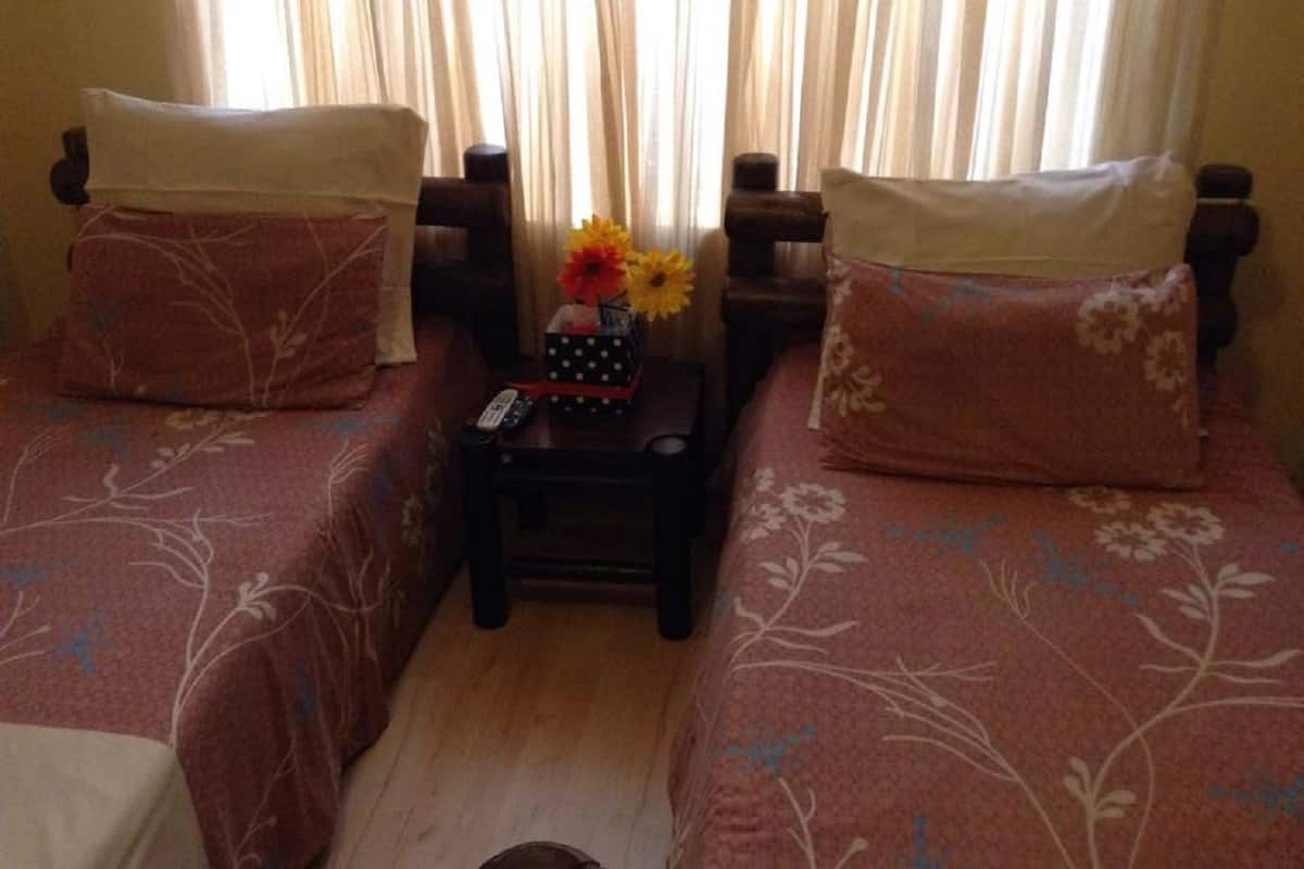 A room with two beds, each with a floral-patterned bedspread and matching pillows. A small table between the beds holds a vase with flowers and a remote control.