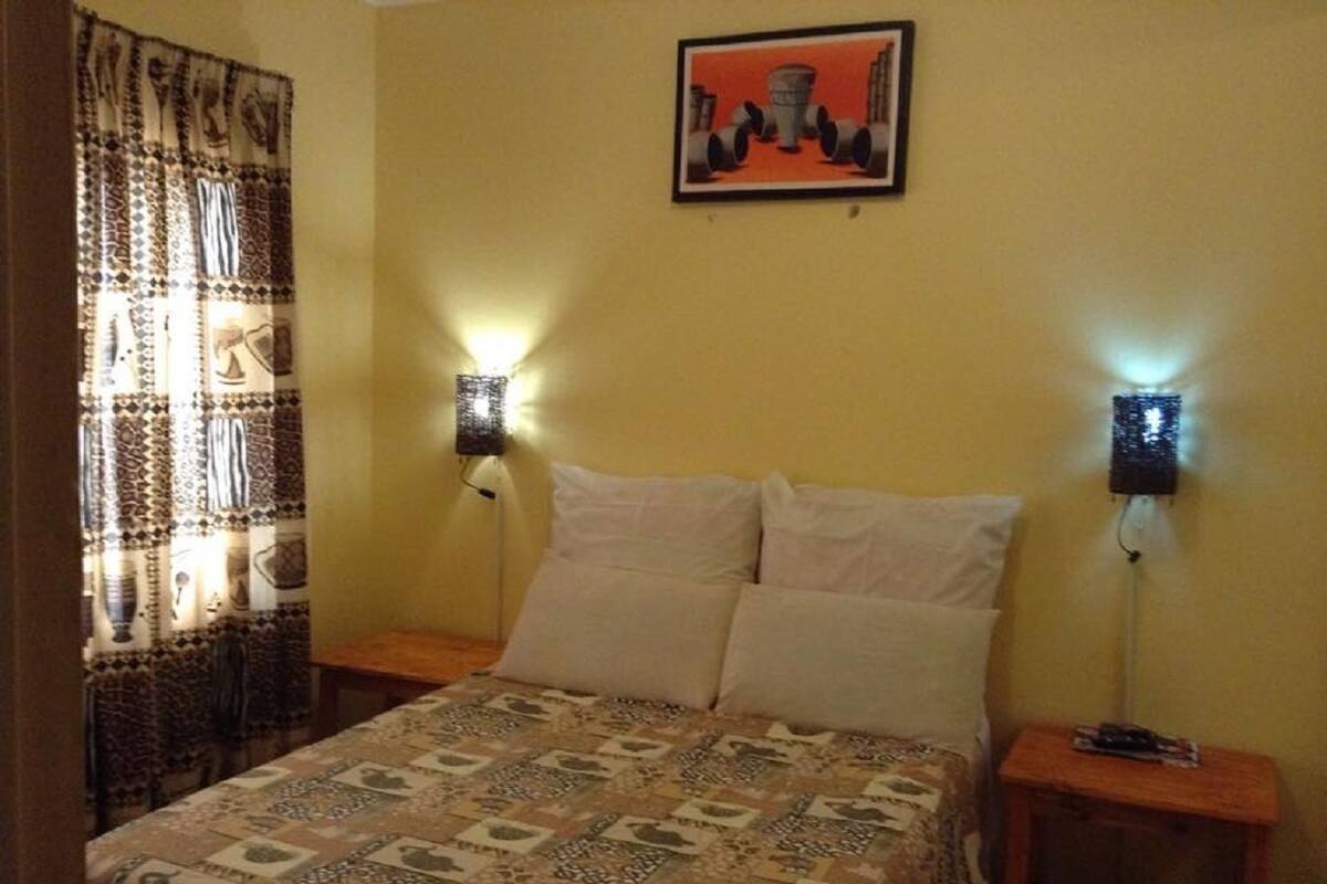 A bedroom with a bed, two bedside tables, a wall-mounted lamp, and a curtain with a patterned design.