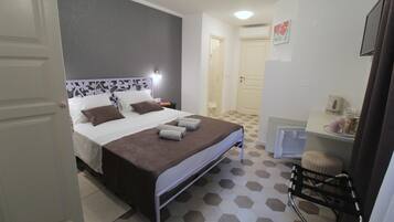 A hotel room with a bed, a bedside table, a chair, and a small desk with a mirror.