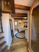 Een slaapkamer met een bed, nachtkastje, lamp, raam en een houten trap.