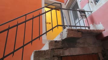 A staircase with a metal railing leading to a yellow door, surrounded by orange and pink buildings with white shutters.