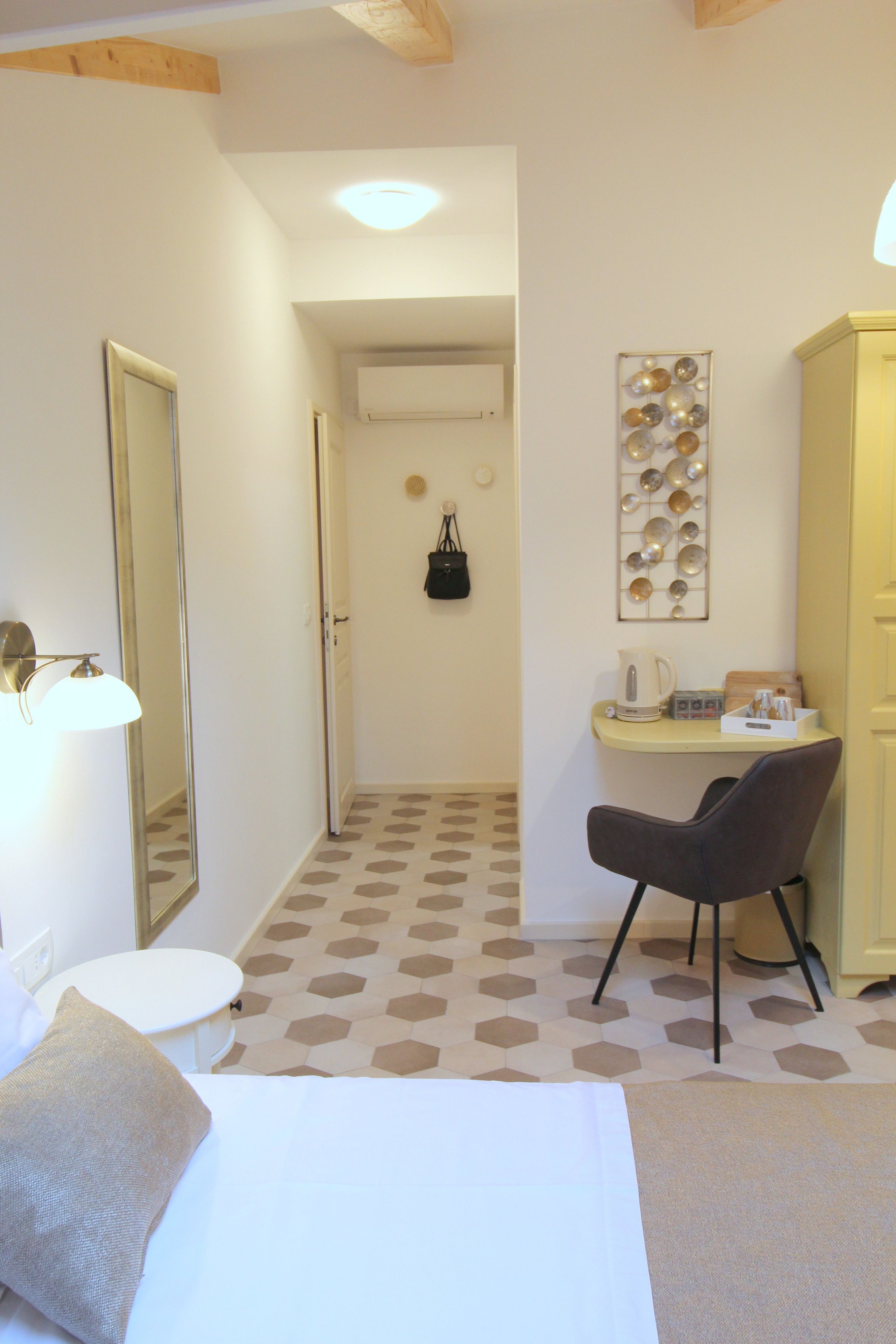 A hotel room with a bed, a desk, a chair, a mirror, a wardrobe, and a wall-mounted light fixture.