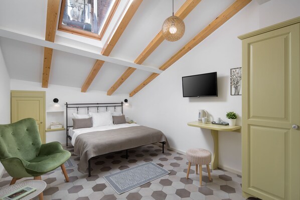 Un dormitorio con una cama, un sillón verde, una mesita, un televisor y una ventana con vigas de madera.