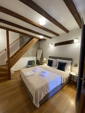 A bedroom with a large bed, wooden beams, a staircase, a small bedside table, and a nightstand. - Noemi's rooms (Rovinj)