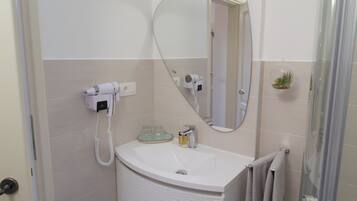 Un baño con lavamanos blanco, espejo, secador de pelo y ducha.