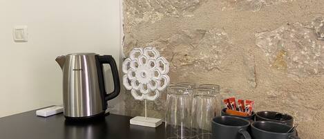 Een aanrecht met een roestvrijstalen waterkoker, een koffieapparaat en twee mokken. Ook staan er verschillende glazen en een decoratief wit wandobject.