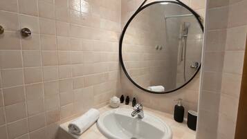 A bathroom with a white sink, a round mirror, and a handheld showerhead.