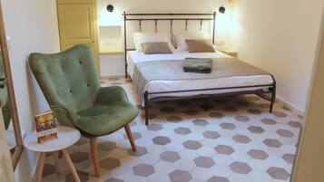 Un dormitorio con un sillón verde, una cama con ropa blanca y un suelo de patrón hexagonal.