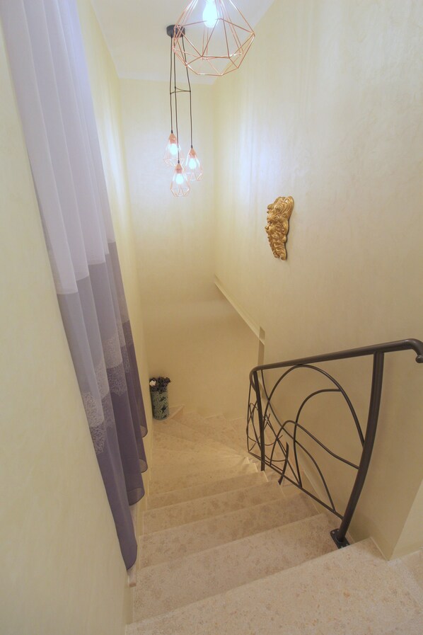 A staircase with a metal railing, a wall-mounted light fixture, and a decorative wall piece. - Noemi's rooms (Rovinj)