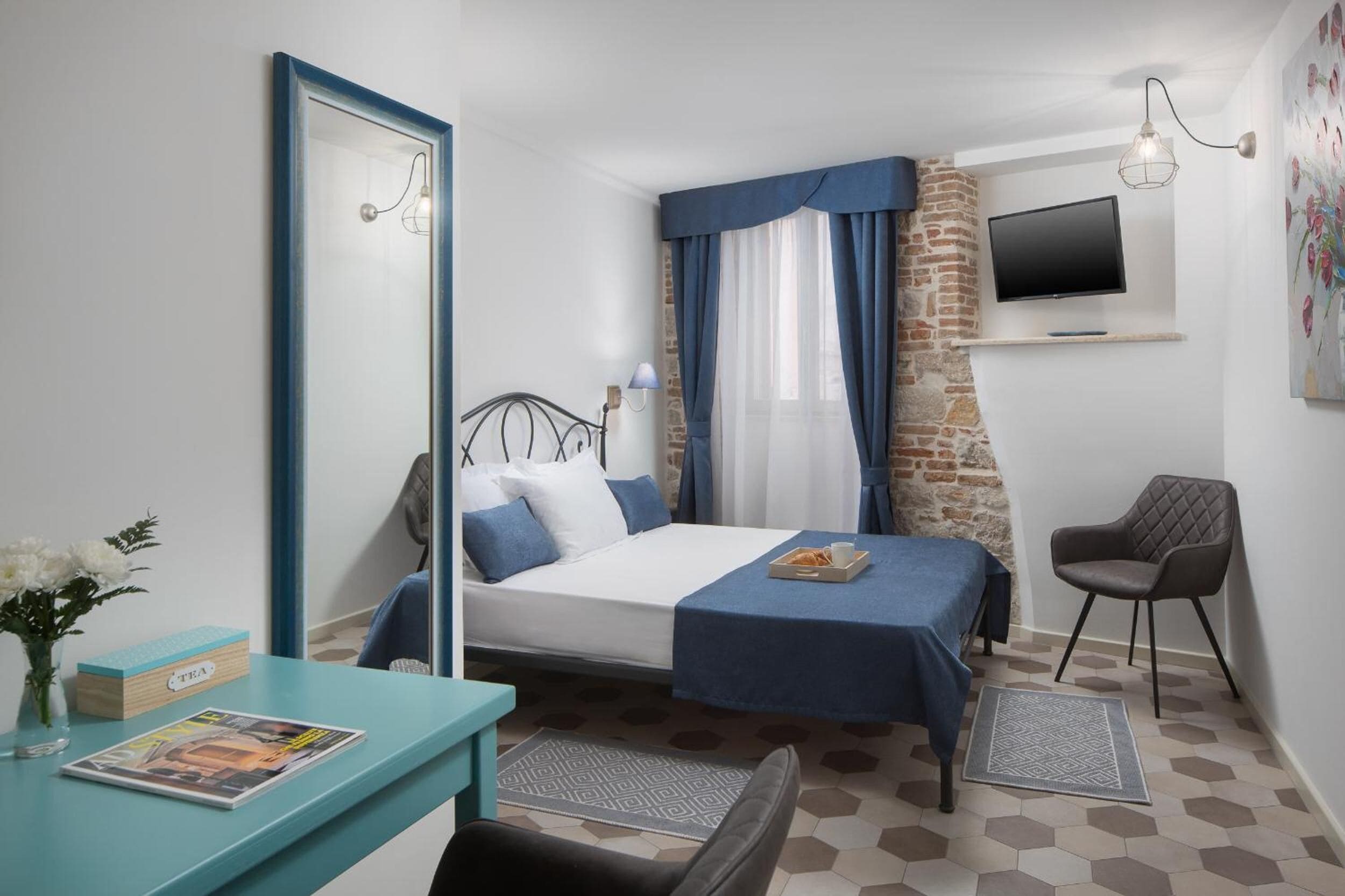 Un dormitorio con cama, escritorio, silla, televisión y ventana con cortinas.