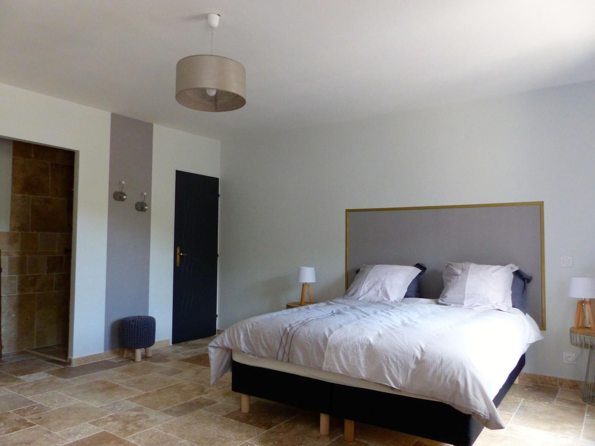 A bedroom with a bed, a door, a wall-mounted light fixture, and a small stool.