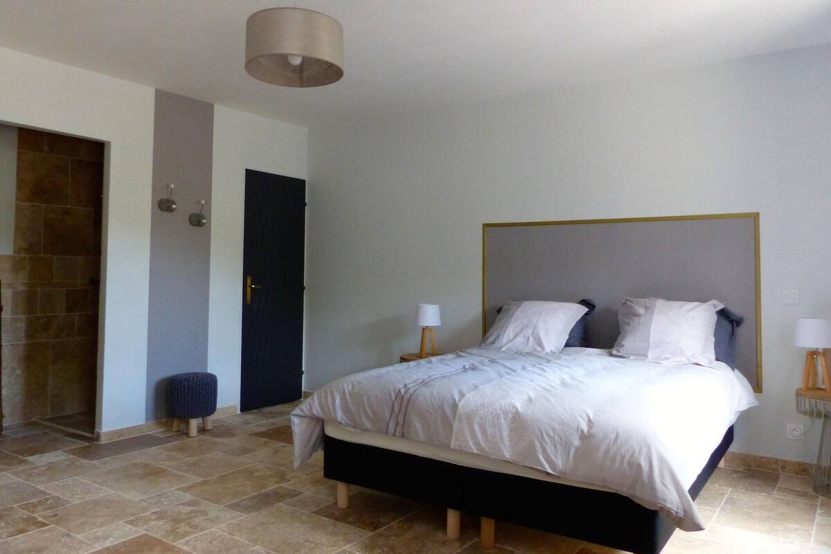 A bedroom with a bed, a door, a wall-mounted light fixture, and a small stool.