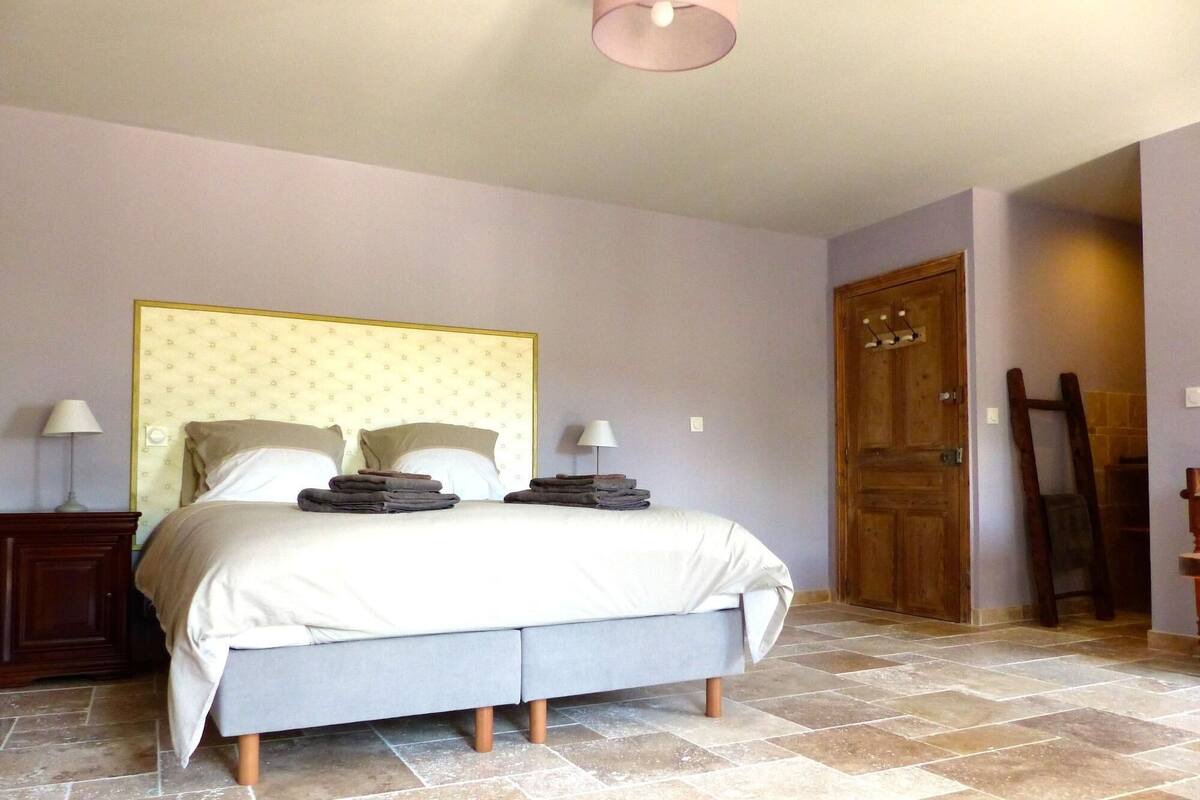 A bedroom with a bed, two bedside tables, a wooden door, and a tiled floor.