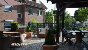 Ein Außenbereich mit Terrasse, Ziegelmauern, Blumentöpfen, Korbmöbeln und einem überdachten Sitzbereich.