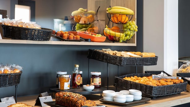 Un buffet proposant une variété d’aliments, notamment du pain, des pâtisseries, des fruits et des condiments.