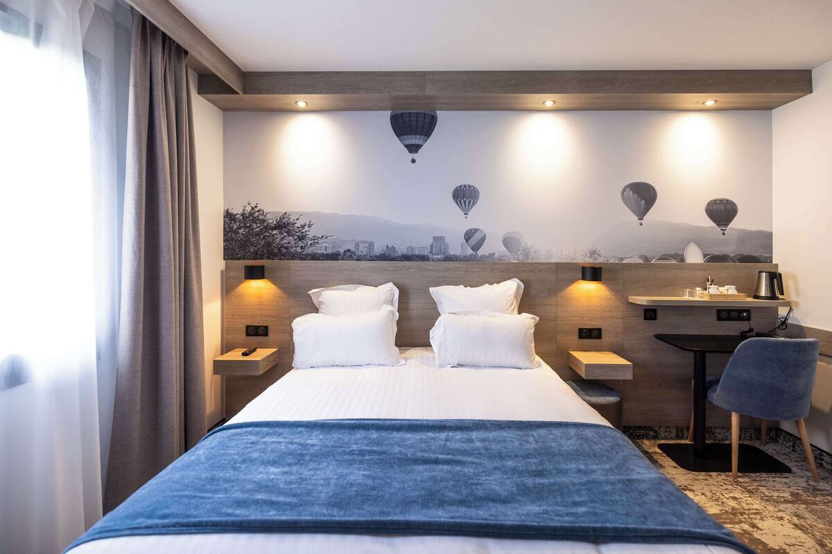 A hotel room with a bed, two bedside tables, a desk, a chair, and a mural of hot air balloons on the wall.
