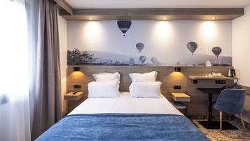 A hotel room with a bed, two bedside tables, a desk, a chair, and a mural of hot air balloons on the wall.