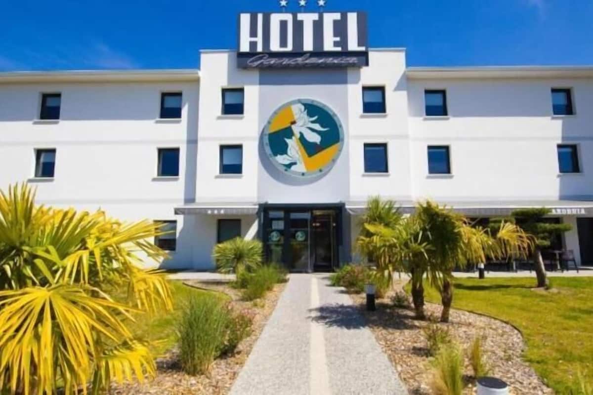 A hotel with a central entrance, a logo above the entrance, and a well-maintained lawn with palm trees.