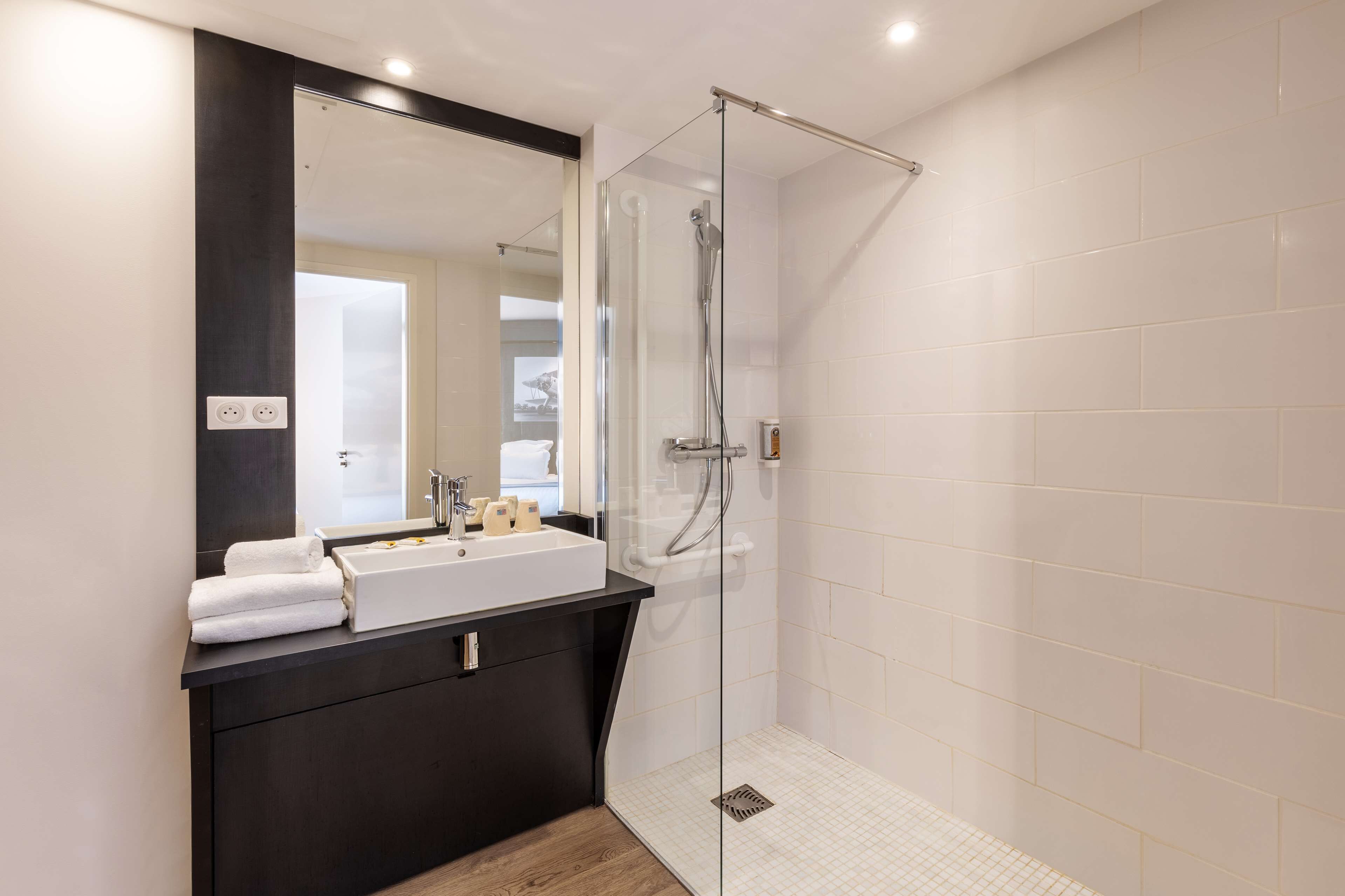 A modern bathroom with a glass-enclosed shower, a large mirror, and a dark countertop.