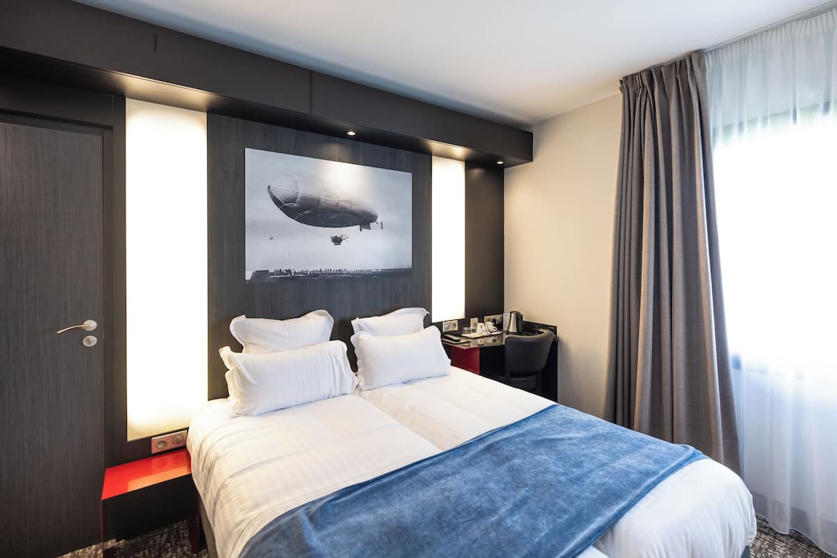 A modern hotel room with a large bed, a desk, and a wall-mounted artwork of a zeppelin.