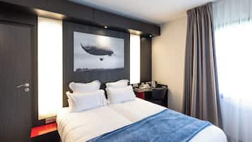 A modern hotel room with a large bed, a desk, and a wall-mounted artwork of a zeppelin.