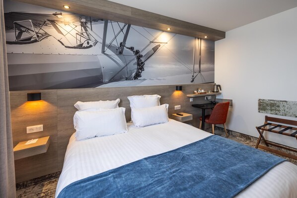 A hotel room with a large bed, a desk, a chair, and a wall-mounted artwork.