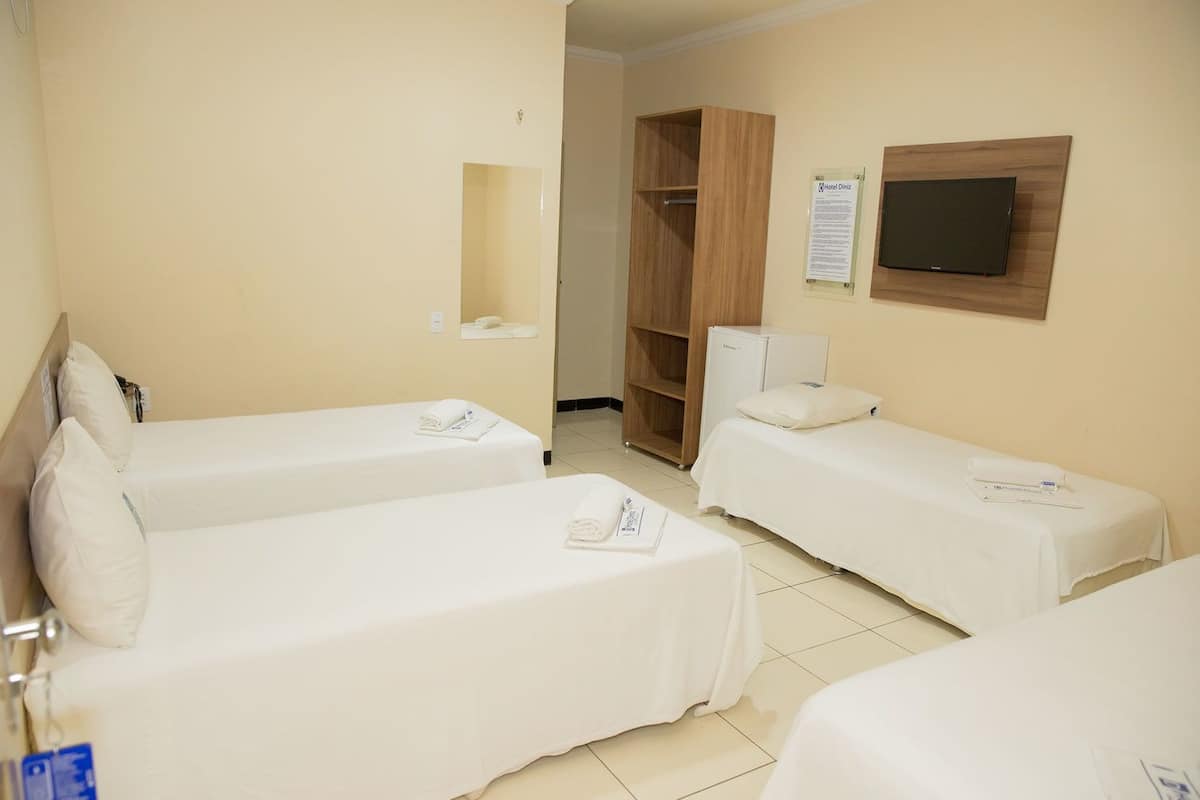 A hotel room with two single beds, a wooden wardrobe, a small refrigerator, and a flat-screen TV mounted on the wall.