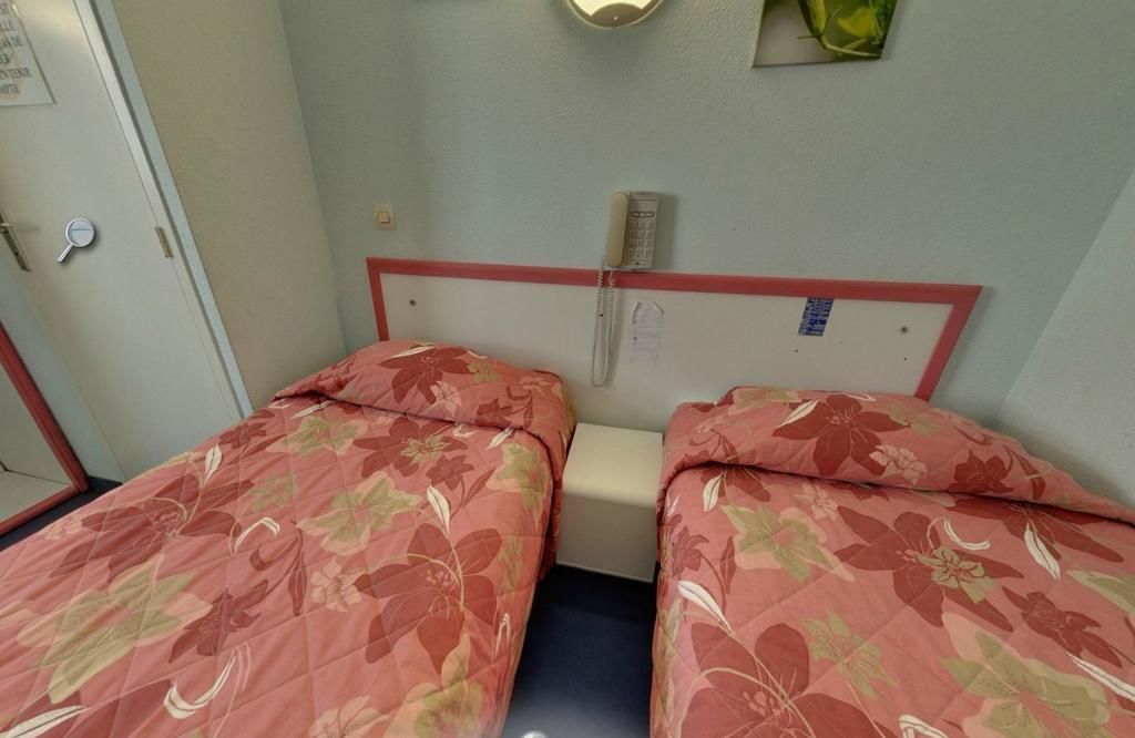 Een kamer met twee bedden, elk voorzien van beddengoed met bloemenprint, een klein nachtkastje, een wandtelefoon en een deur met een handvat.