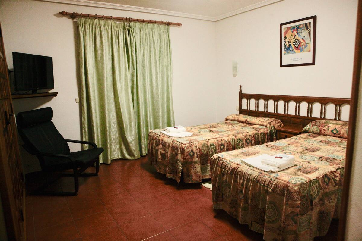 A room with two beds, a chair, a television, and a curtain.