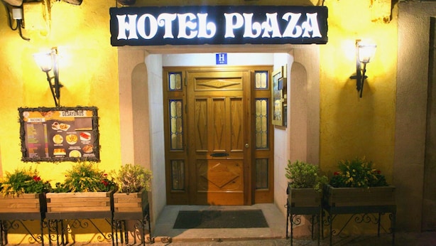 A hotel entrance with a sign reading "HOTEL PLAZA," a wooden door, and a menu board to the left. - Hotel Plaza (Riaza)
