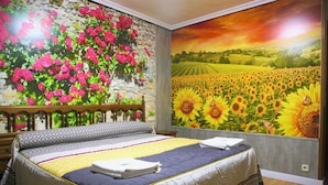 A bedroom with a large bed, a stone wall with a floral mural, and a sunset mural on the opposite wall. - Hotel Plaza (Riaza)