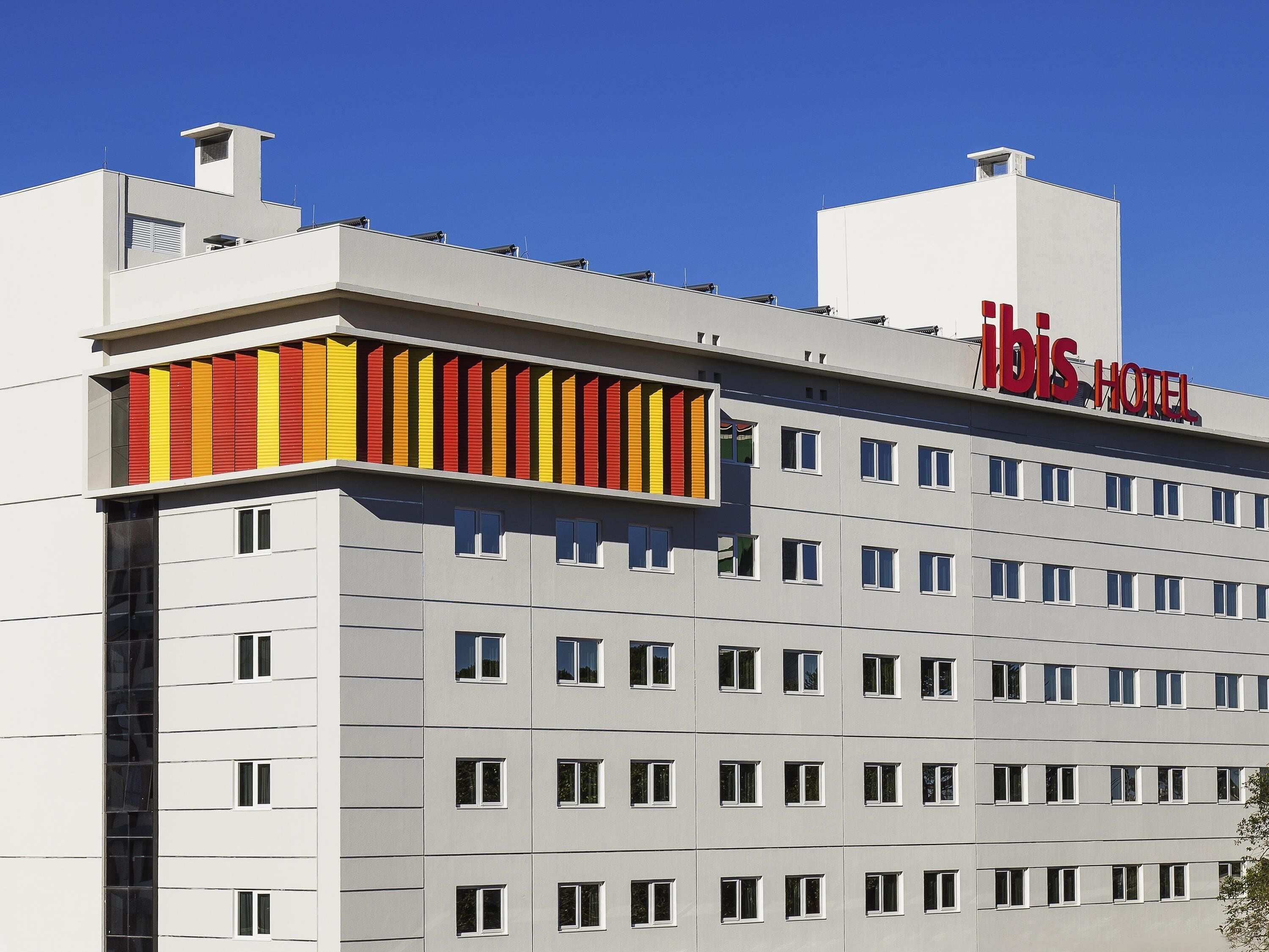 A hotel building with a modern design, featuring a prominent 'ibis Hotel' sign on the roof.