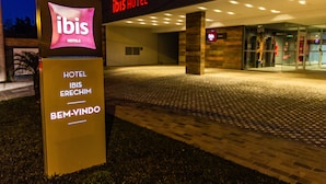 Entrada de un hotel con un cartel que dice 'ibis HOTEL ERECHIM BEM-VINDO'.