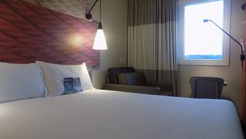 Habitación de hotel con una cama grande, un escritorio, una silla, una lámpara y una ventana con cortinas.