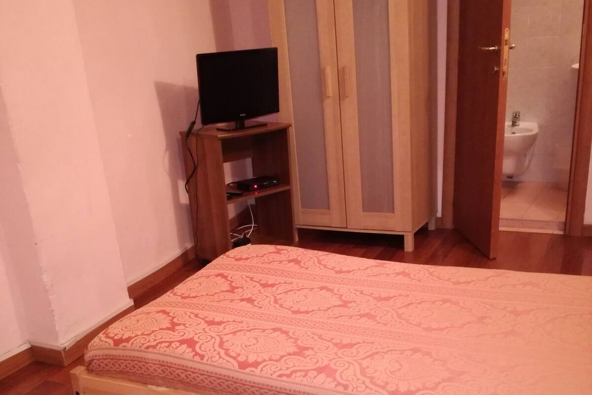 Ein Schlafzimmer mit einem Bett, einem Kleiderschrank, einem Fernseher und einem durch eine offene Tür einsehbarer Badezimmer.