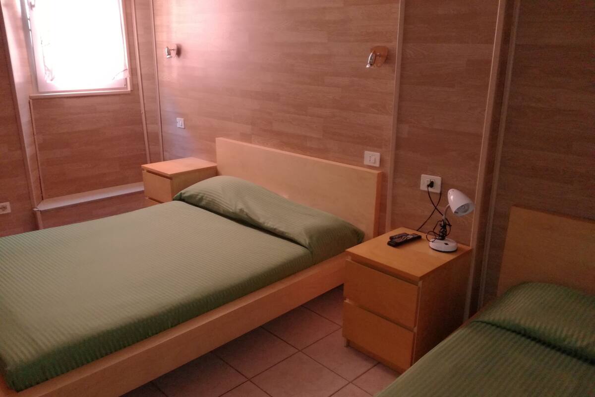 Ein Zimmer mit einem Einzelbett, einem Nachttisch mit Lampe und einem kleinen Tisch.