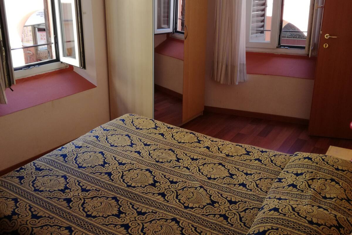 Ein Schlafzimmer mit Bett, Kleiderschrank, Fenster mit Rollläden und Tür.