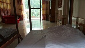Ein Hotelzimmer mit einem Bett, einem roten Sessel und Blick ins Freie durch ein großes Fenster.