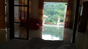 Ein Zimmer mit einem Bett, einem roten Sessel und Blick auf einen Garten durch eine Glastür.