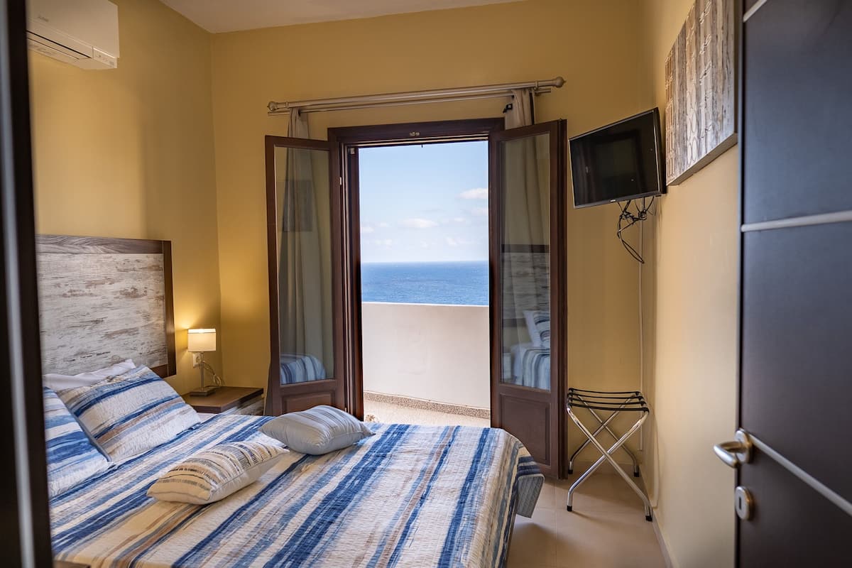 Une chambre d’hôtel avec un lit, une table de chevet, une télévision et une vue sur la mer.