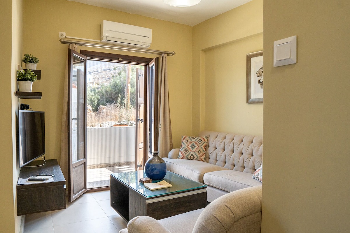 Un salon comprenant un canapé, une table basse en verre, un téléviseur et une porte-fenêtre coulissante donnant sur un balcon.
