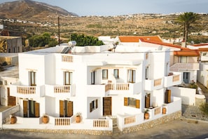 Un edificio blanco con varios balcones, base de piedra y montañas al fondo.