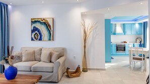 A modern living room with a beige sofa, a blue vase, and a painting on the wall. - Theoxenia Suites & Apartments (Kasos)