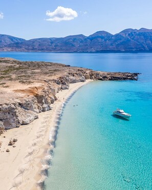 Un paisaje costero con una playa despejada, afloramientos rocosos y un barco en el agua.