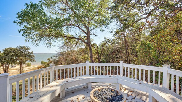 Une terrasse en bois avec une balustrade blanche, un grand bac à fleurs et une vue sur la plage et l’océan.