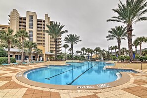 A swimming pool with a 4-foot depth marker, surrounded by palm trees and a multi-story building with balconies. - Beachfront Destin Condo w/ Pool & Harbor View! (Destin)